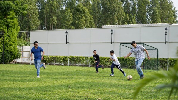 A grassy field with a soccer goal, trees, and a building in the background. - White Mist by NAVA (Devanahalli)