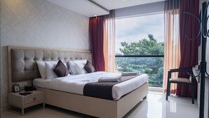 Un dormitorio moderno con una cama grande, una mesita de noche, una silla y vistas al verdor exterior.