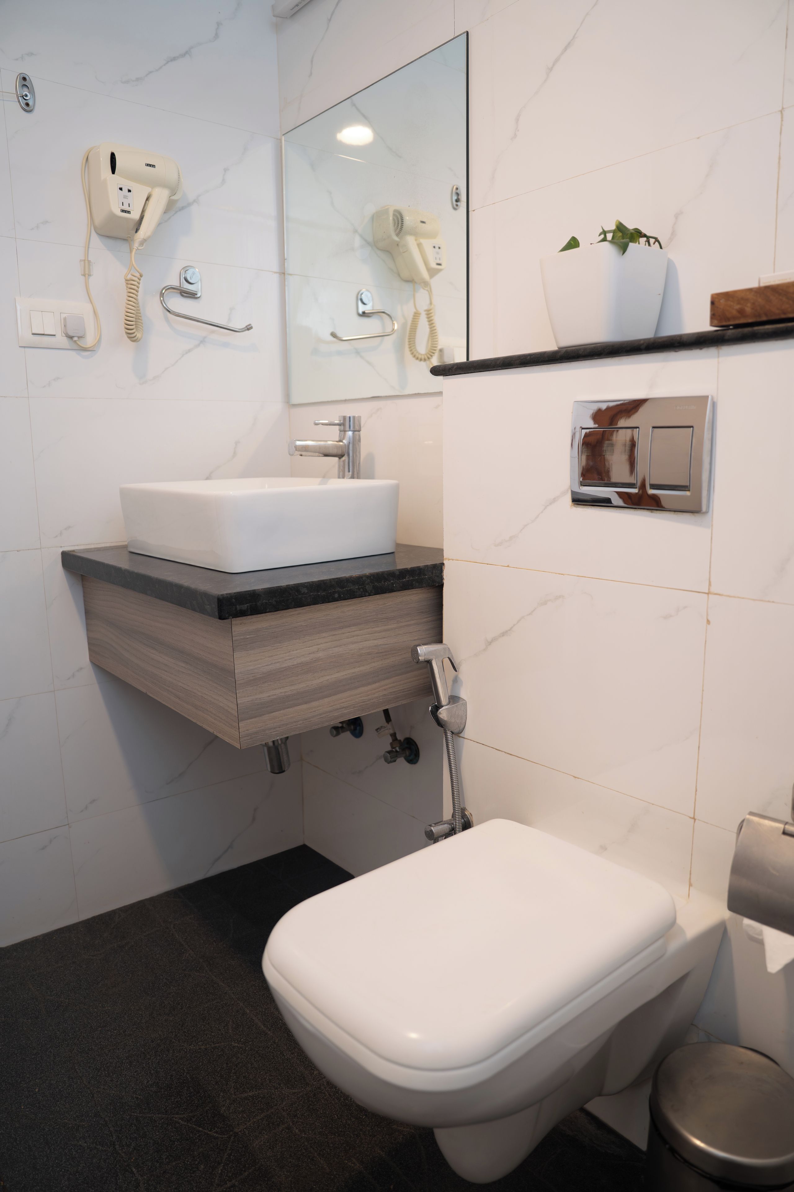 Een moderne badkamer met een witte wastafel, een spiegel, een haardroger en een toilet.