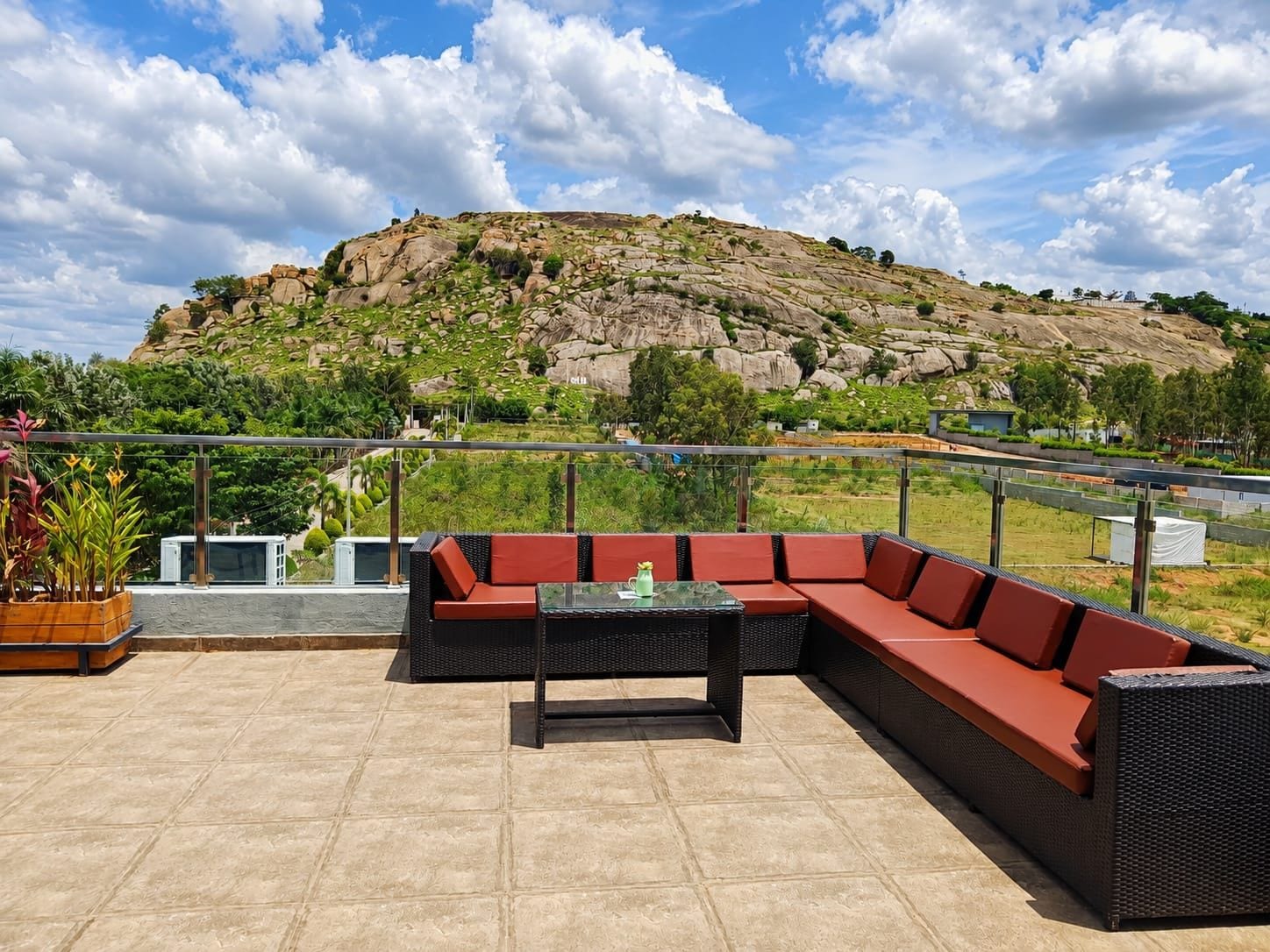 A rooftop terrace with outdoor seating, a view of a rocky hill, and a clear sky.