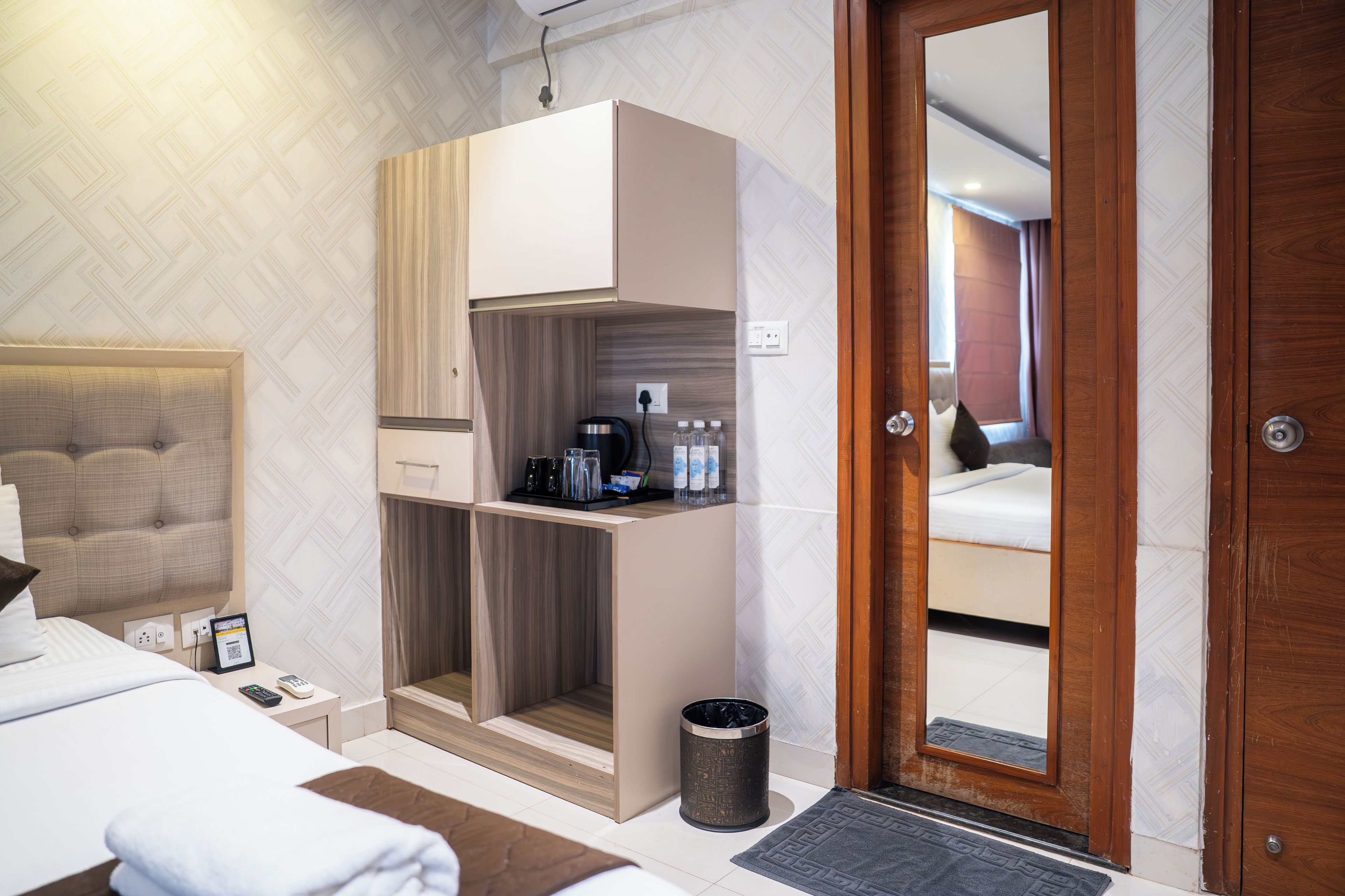 Une chambre d’hôtel comprenant un lit, une petite kitchenette, une poubelle et une porte donnant sur une autre pièce.
