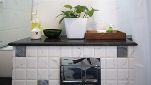Een keukentafel met een witte betegelde achterwand, een potplant, een witte vaas met bamboe-verdamper, een groene kom en een houten dienblad met een groene fles.