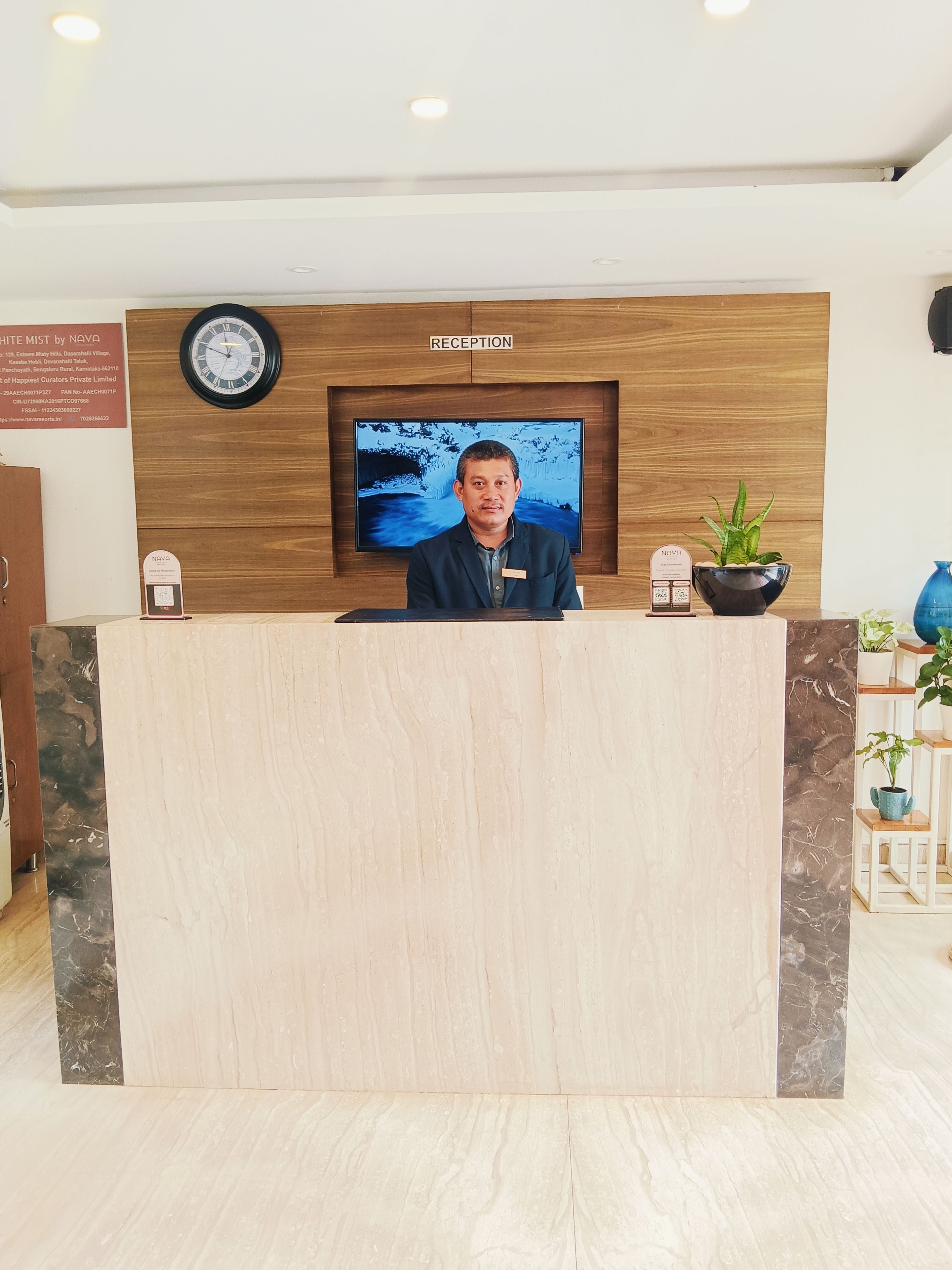 A reception desk with a wooden backdrop, a clock, and a television screen displaying a snowy landscape.