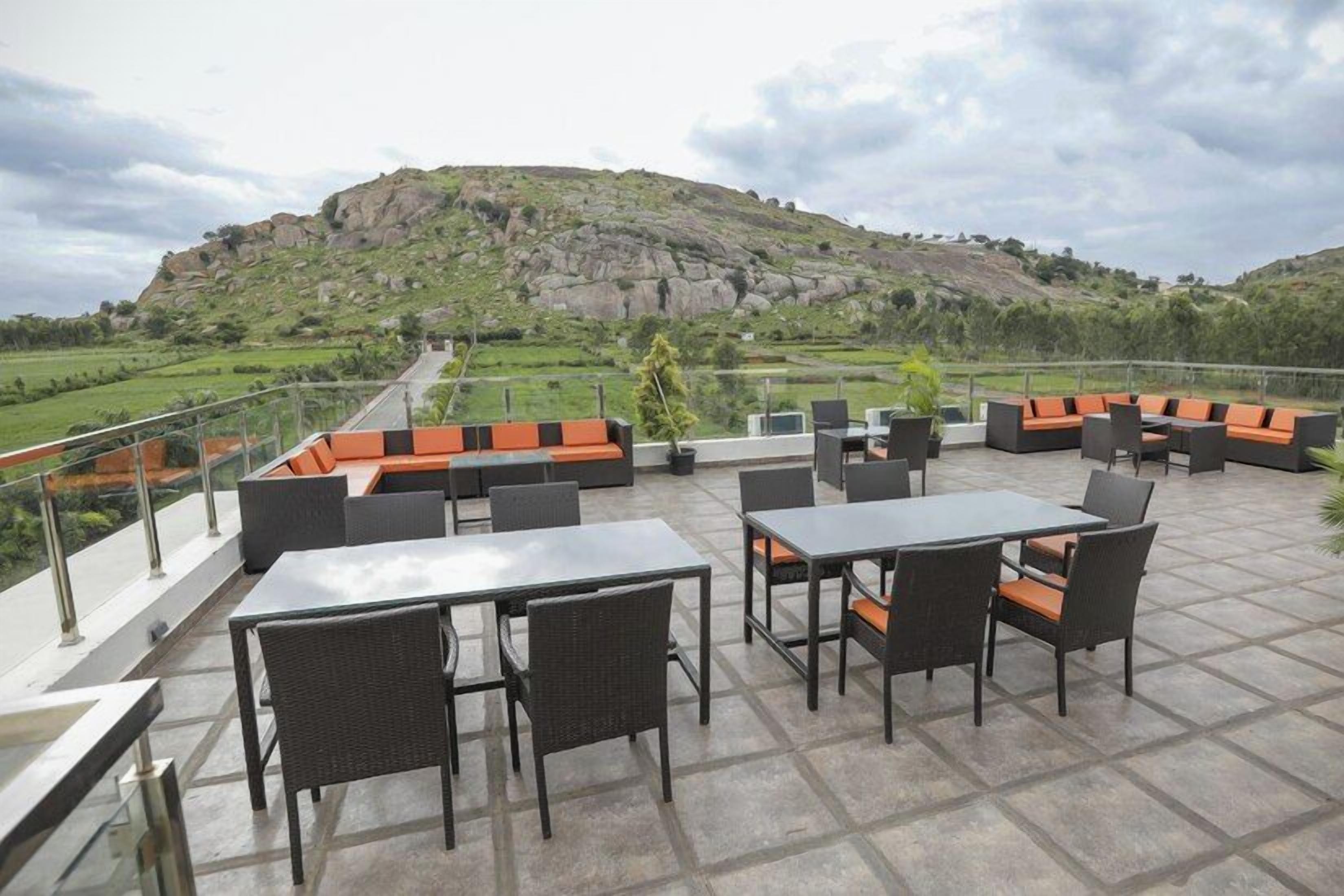 An outdoor seating area with tables and chairs, overlooking a hilly landscape.
