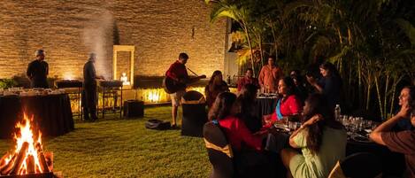 Une réunion en plein air avec un foyer, des tables et des personnes qui prennent leur repas.