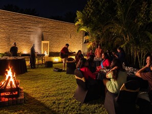 An outdoor gathering with a fire pit, tables, and people dining. - White Mist by NAVA (Devanahalli)