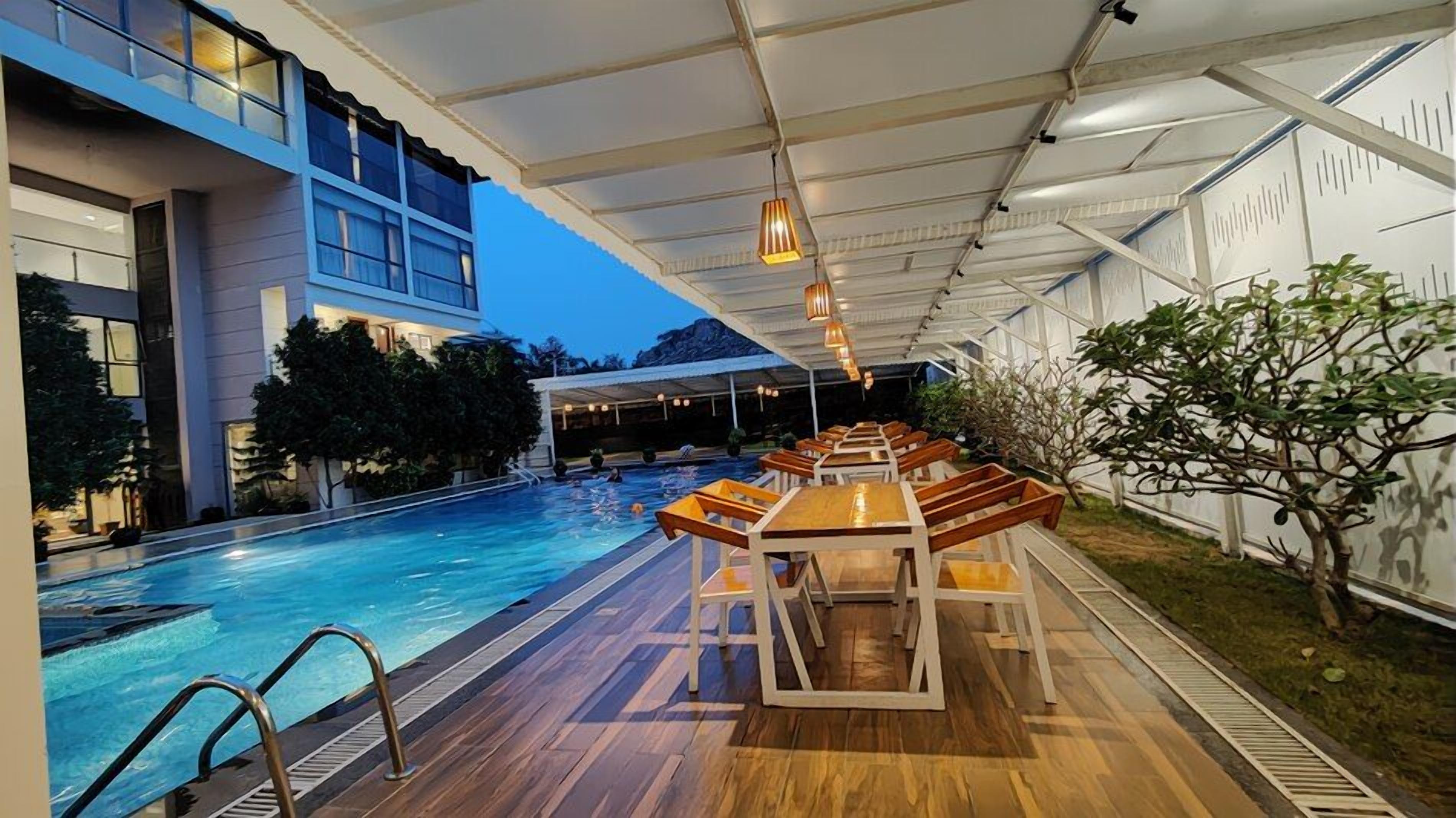 Una piscina interior con mobiliario de cubierta de madera y un área techada con luces colgantes.