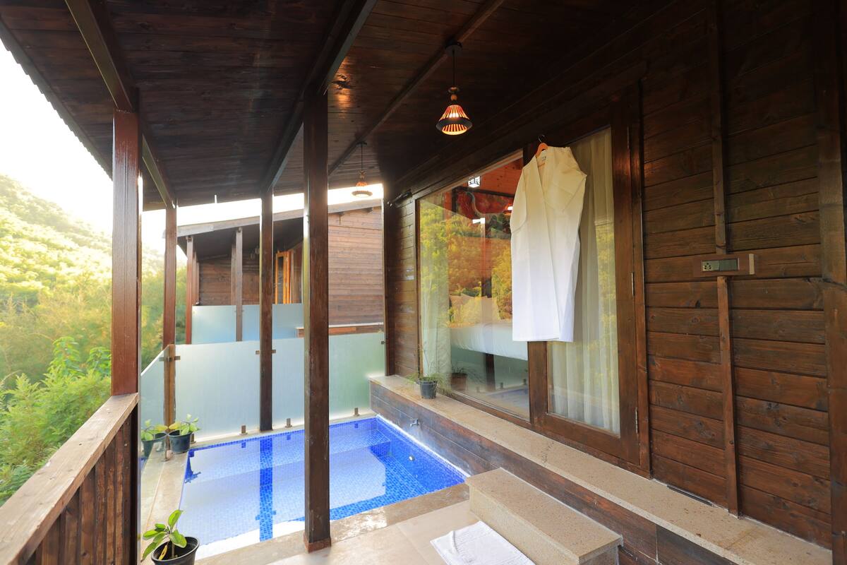 A wooden cabin with a glass-enclosed pool, wooden deck, and a view of the surrounding greenery.