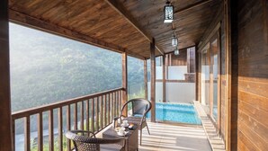 Un balcón de madera con piscina, sillas de mimbre y una mesa con cafetera.