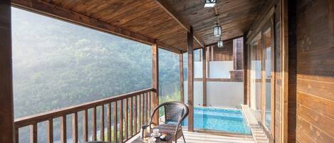 Un balcon en bois avec une piscine, des fauteuils en osier et une table sur laquelle se trouve une cafetière.