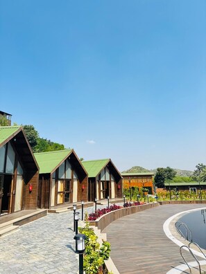 A hotel with modern architecture, featuring a pool area with a wooden deck and a landscaped garden. - Vasant Kunj Nature Resort (Udaipur)