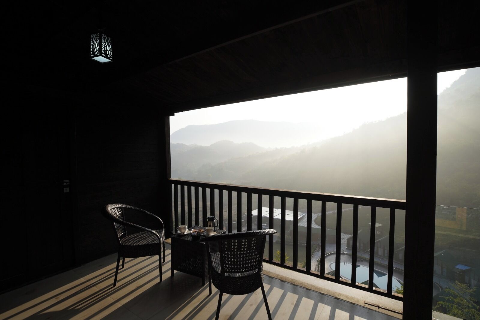 A balcony with two wicker chairs, a small table, and a view of a misty mountain landscape.