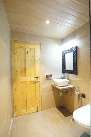 A bathroom with a wooden door, a white sink, a mirror, and a toilet. - Vasant Kunj Nature Resort (Udaipur)