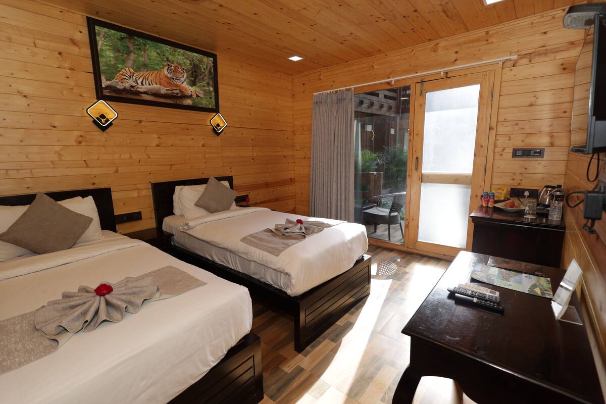 A wooden cabin with two beds, a desk, a chair, a painting of a tiger, and a sliding glass door to a balcony.