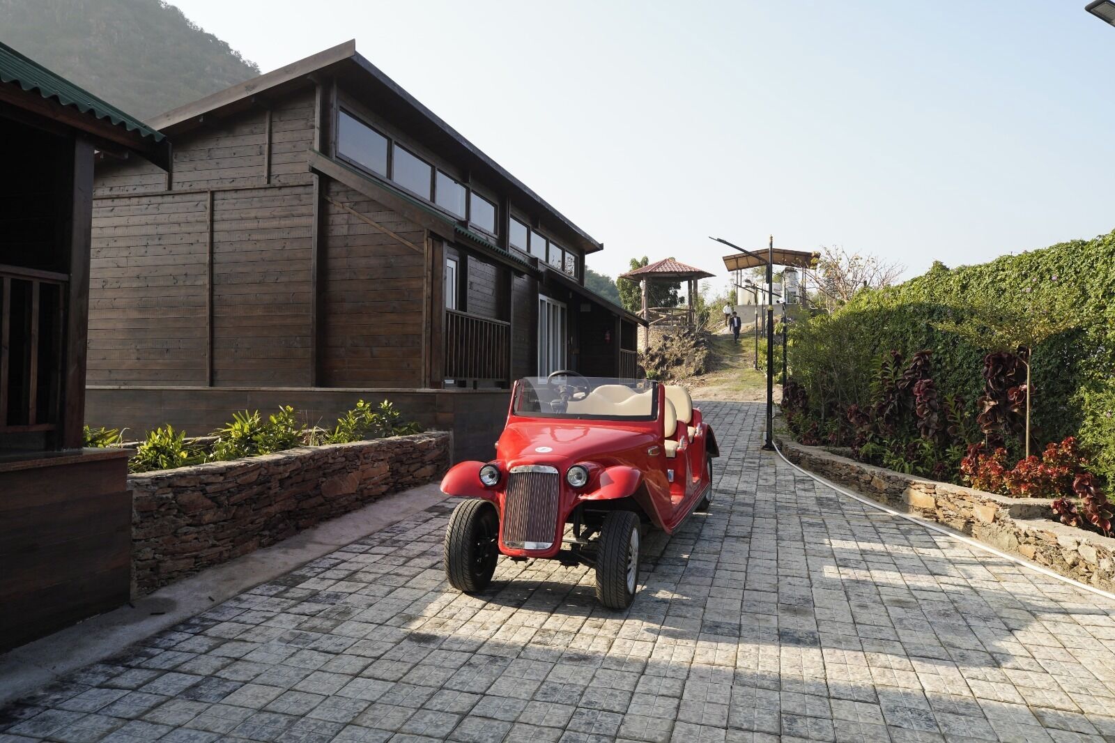 A red vintage car parked on a paved driveway next to a modern wooden house.