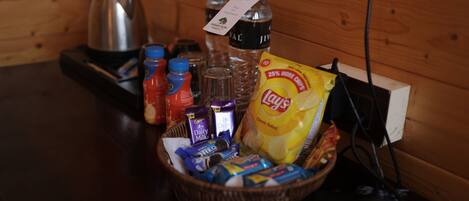 A wooden table with a basket containing snacks, a bottle of water, a bottle of juice, a bottle of milk, and a kettle.