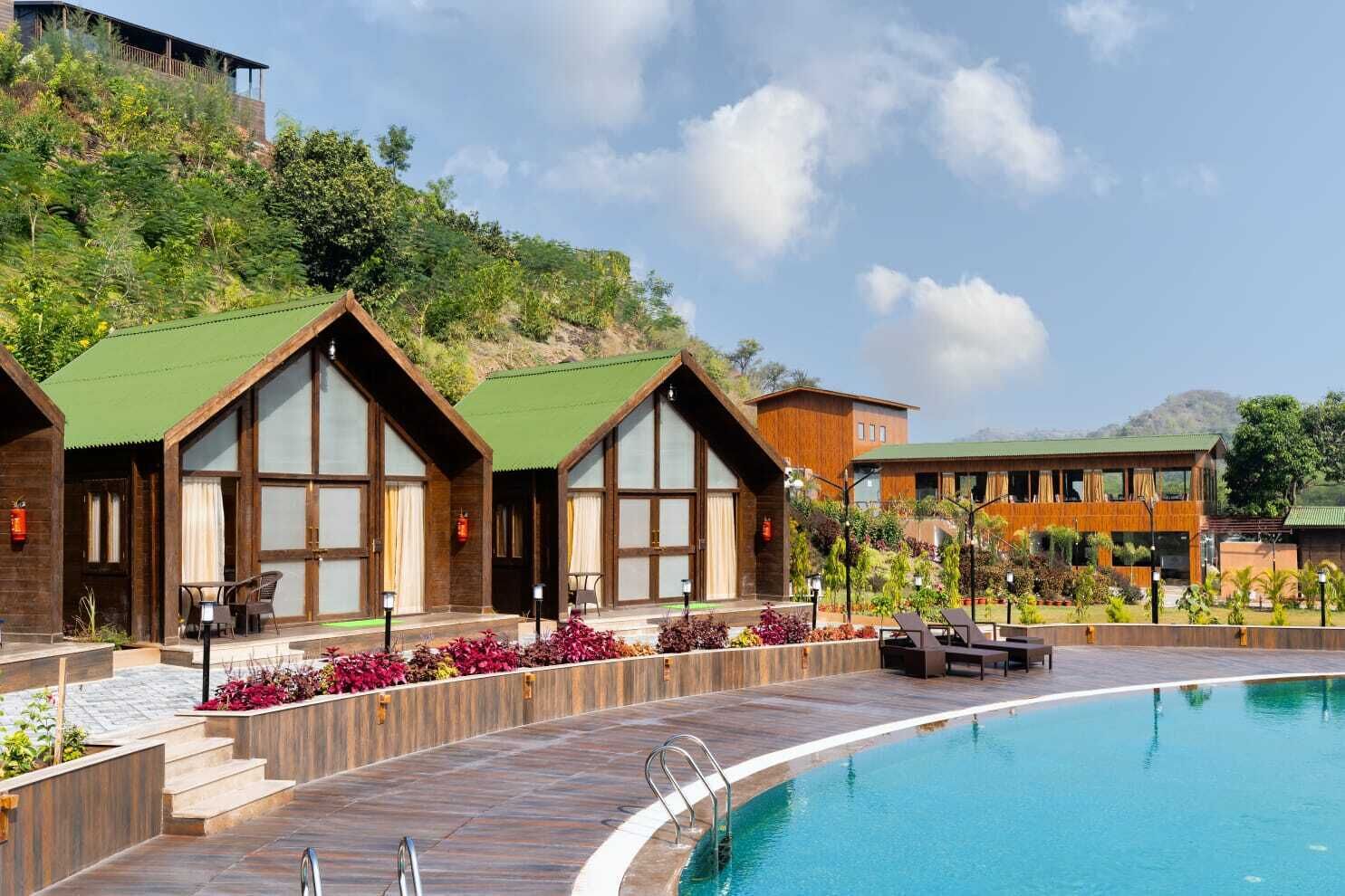 A resort with a swimming pool, wooden cabins with large windows, and a landscaped garden.