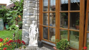A stone statue of a figure, a window with lace curtains, and potted plants with red flowers. - Vacation apartment 85 sqm with terrace (Rottau)