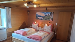 A wooden-paneled bedroom with a bed, a cross on the wall, and a painting of a mountain landscape. - Vacation apartment 85 sqm with terrace (Rottau)