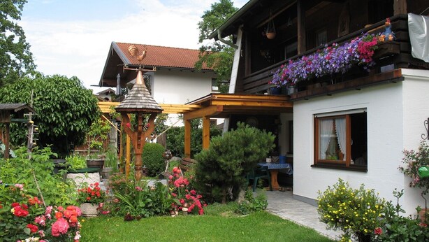 A garden with a gazebo, a white house with a balcony, and various flowers. - Vacation apartment 85 sqm with terrace (Rottau)
