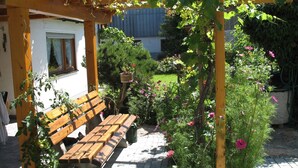 A wooden pergola with a bench, surrounded by potted plants and flowering shrubs. - Vacation apartment 85 sqm with terrace (Rottau)