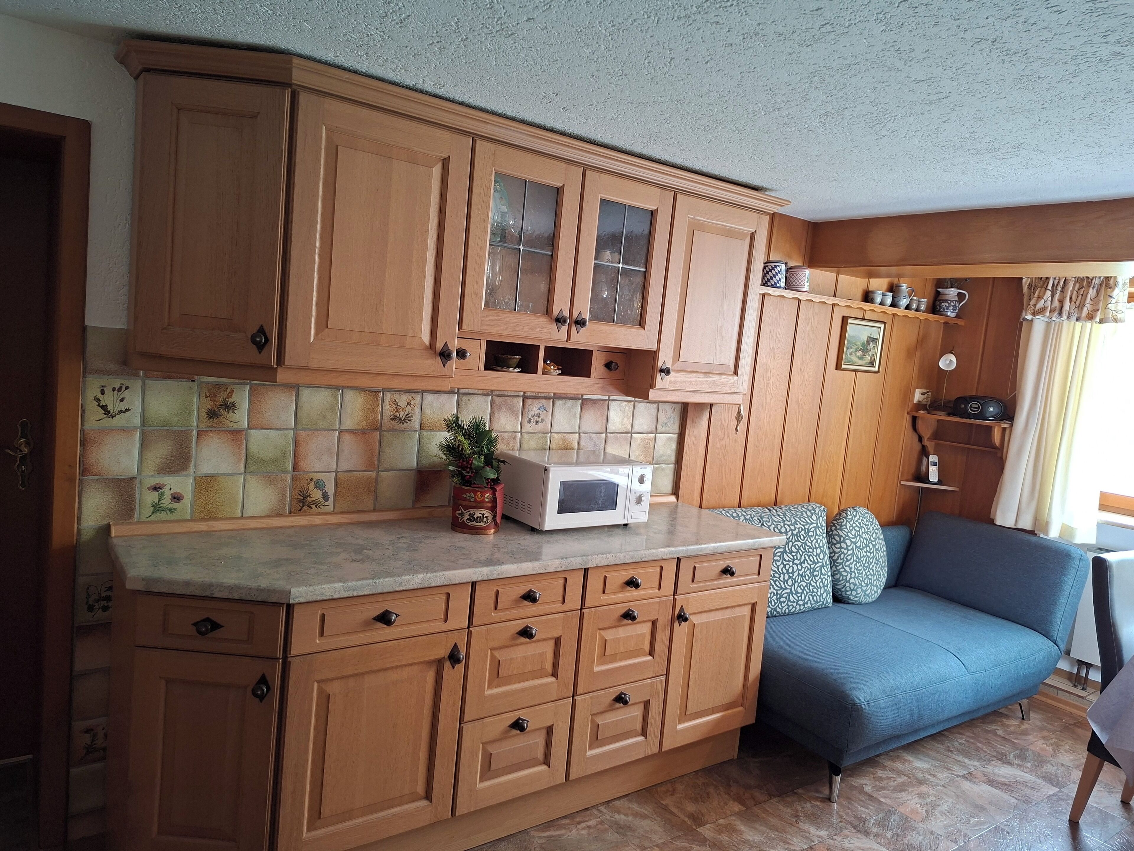 Een keuken met houten kastjes, een magnetron en een blauwe bank.