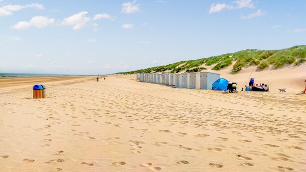 Una spiaggia con file di bagni chimici, un cestino e una tenda allestita sulla sabbia.