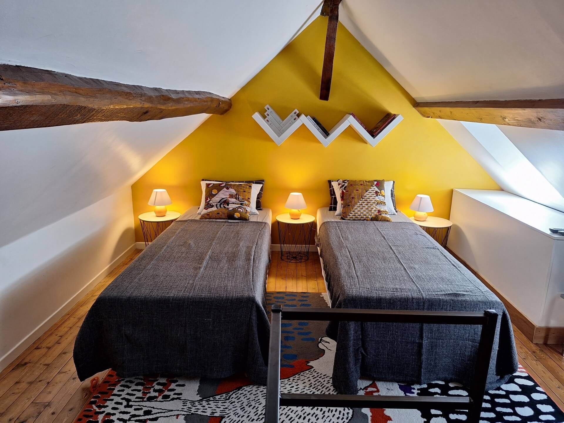 A room with two beds, a wooden ceiling, and a yellow accent wall.