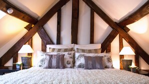 Ein Schlafzimmer mit Gewölbedecke, Holzbalken, einem großen Bett mit floralem Bettbezug, zwei Nachttischlampen und einer kleinen Pflanze auf dem Nachttisch.