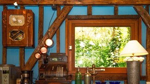 Ein rustikaler Raum mit Holzbalkendecke, einem großen Fenster mit Blick auf Grünflächen, einem alten Telefon, einer Kaffeemaschine und einer Lampe.