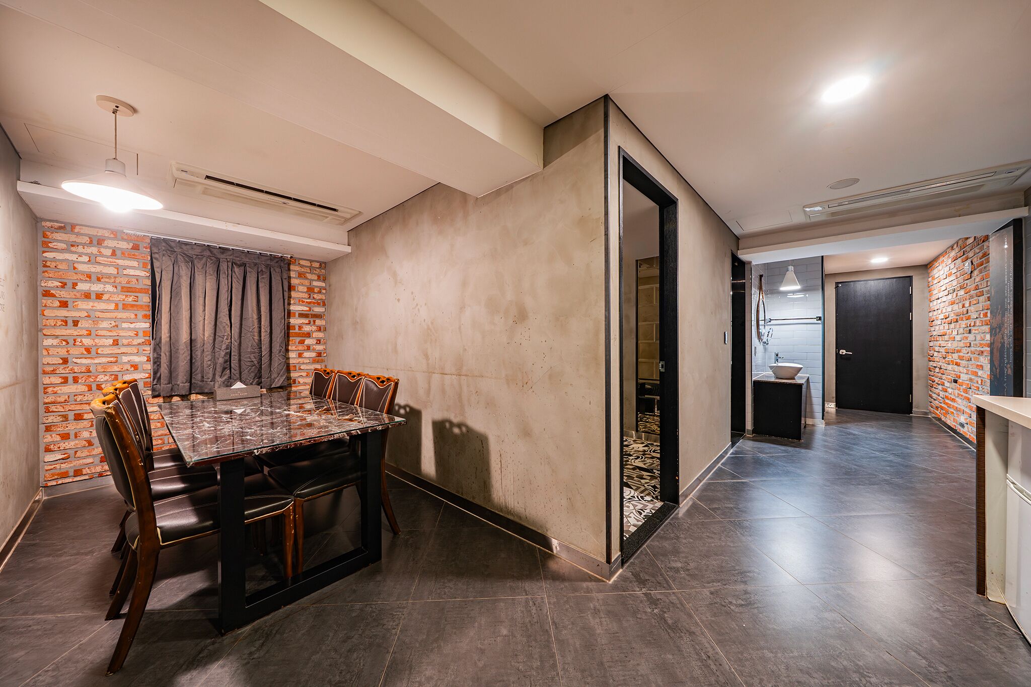Un área de comedor moderna con una pared de ladrillo decorativa, una partición de vidrio y un piso de baldosas oscuras.