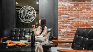 A woman sitting on a black leather couch in a room with a brick wall and a black leather chair. - Jamsil Raum Tourist Hotel (Seoul)