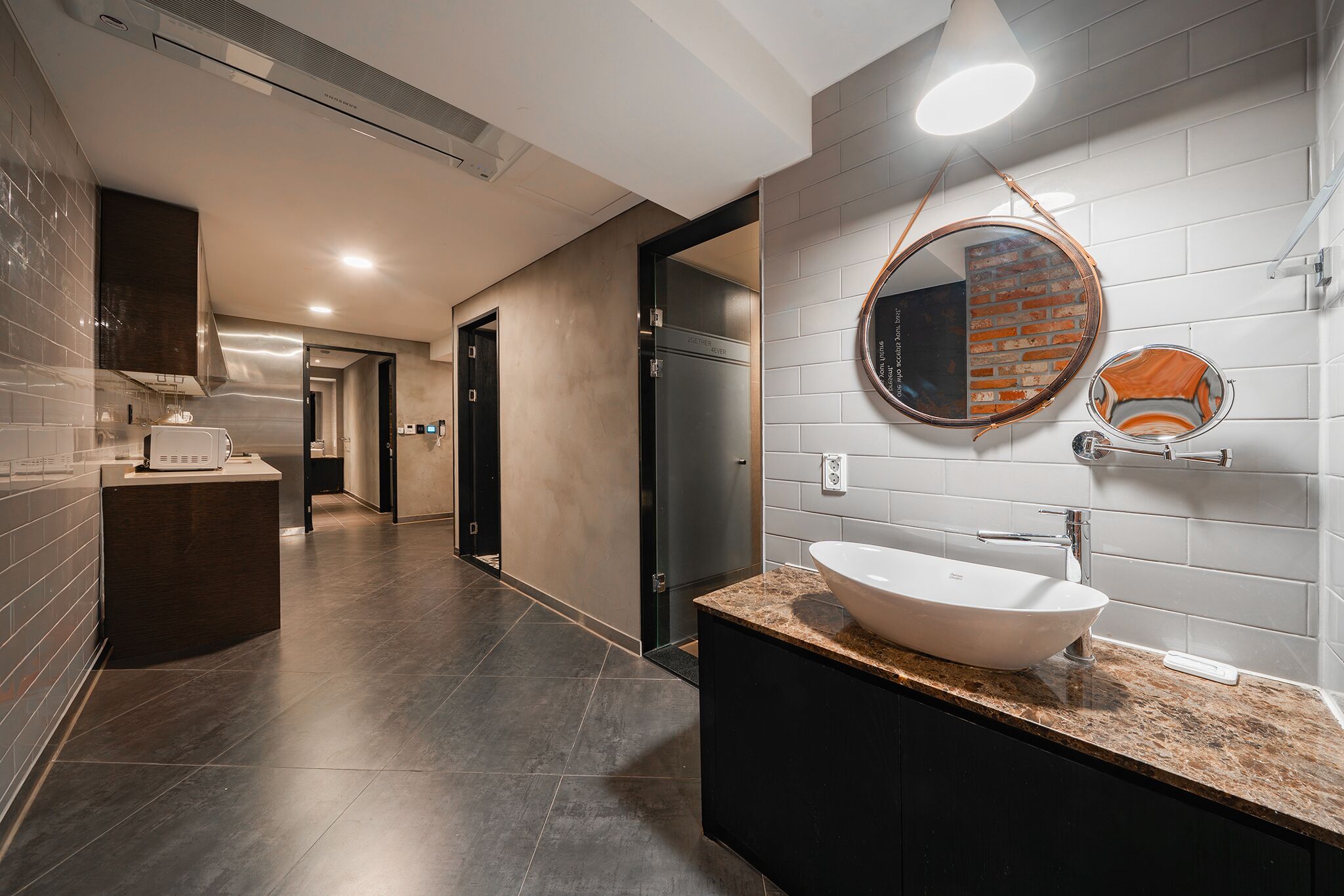 A modern bathroom with a large sink, a round mirror, and a dark-toned vanity.