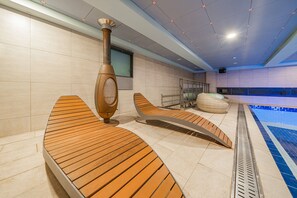 Un moderno espacio de spa con tumbonas de madera, sauna y piscina.