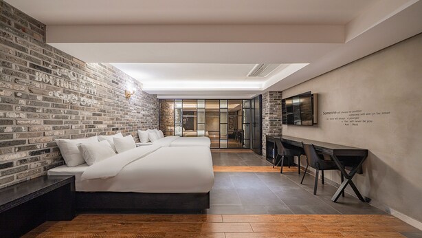 A modern hotel room with a brick wall, a large bed, a desk, and a fireplace. - Jamsil Raum Tourist Hotel (Seoul)