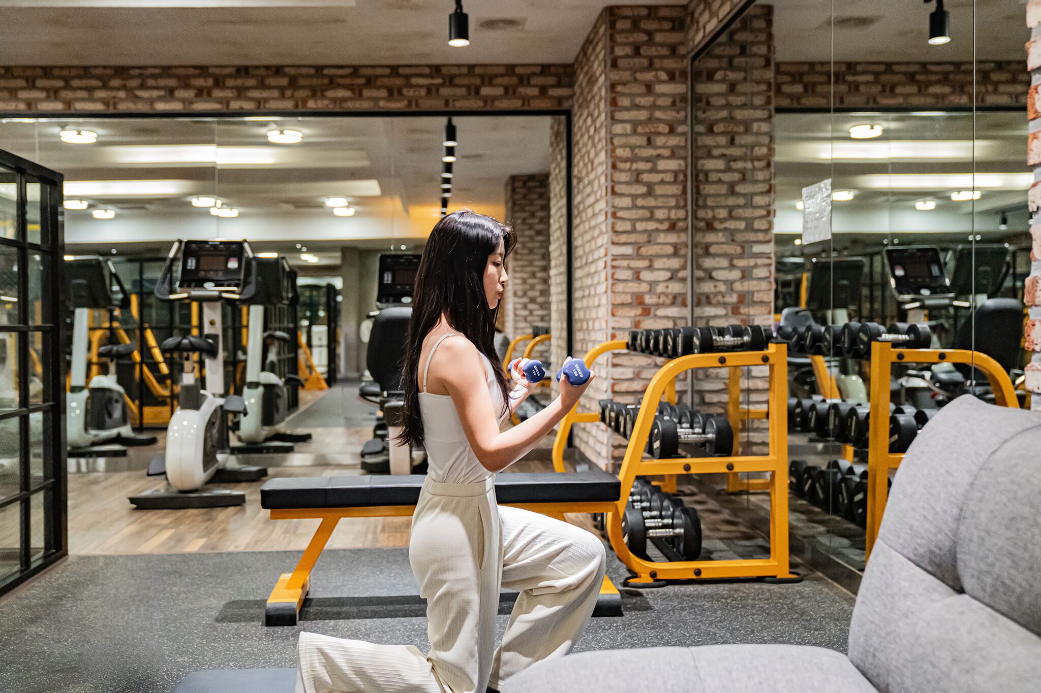 Un gimnasio con equipo de ejercicio, un espejo grande y una pared de ladrillo.