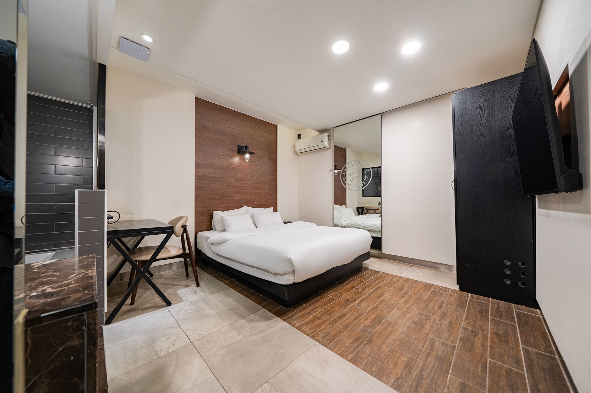 Una habitación de hotel moderna con cama, una mesita, una silla, televisor y aire acondicionado.