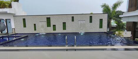 Una piscina con pared texturizada y detalles en ventanas verdes.