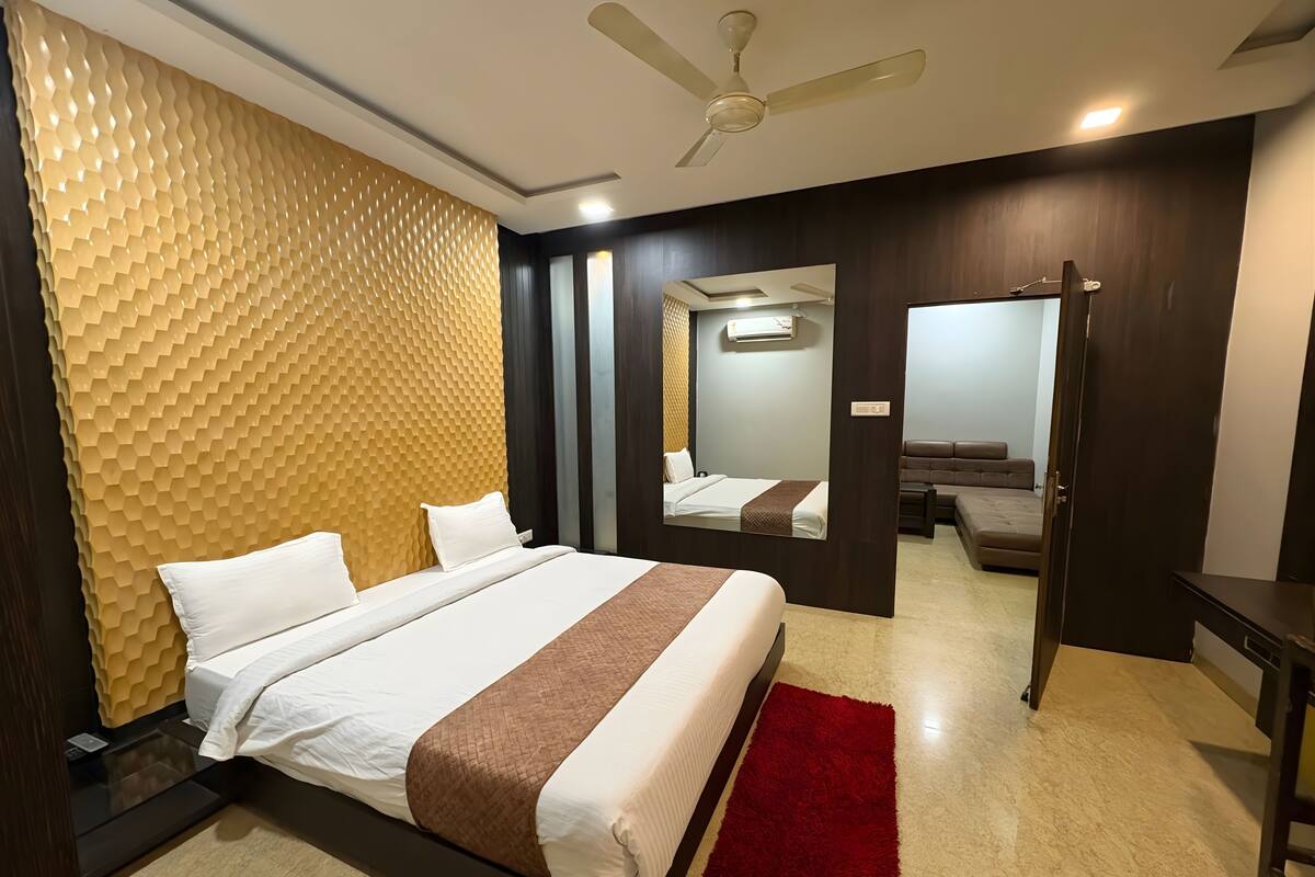 Een moderne hotelkamer met een groot bed, een rood kleed, een plafondventilator en een spiegel die de kamer weerspiegelt.