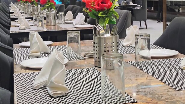 Un restaurante con mesas dispuestas, con servilletas blancas, cubiertos y cristalería, además de flores rojas en jarrones.
