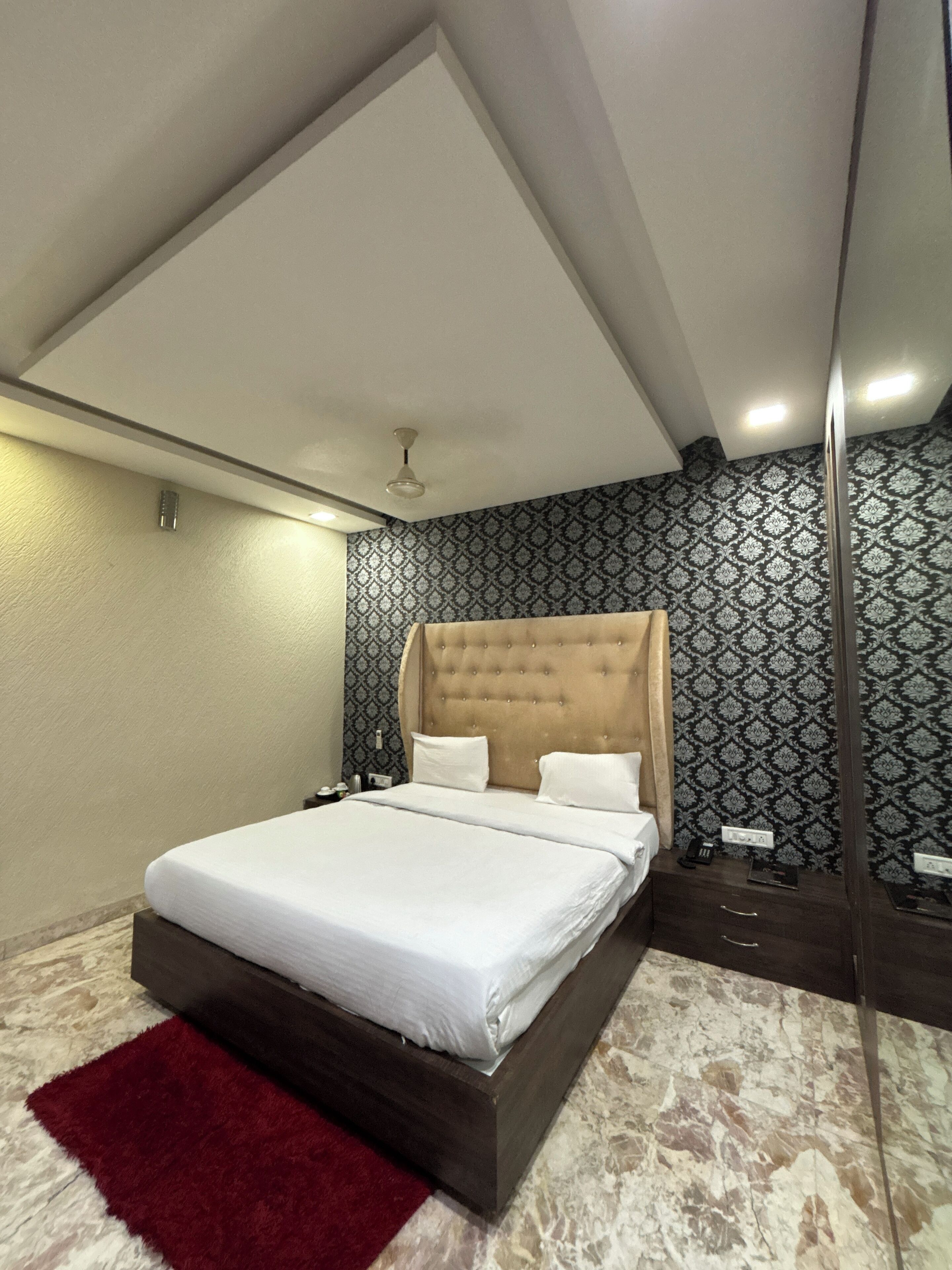 A modern bedroom with a large bed, a ceiling fan, patterned wallpaper, and a marble floor.