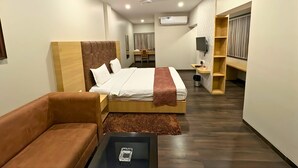 Habitación de hotel moderna con una cama grande, un sofá de cuero marrón, una mesita y un televisor.