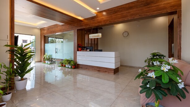 A modern reception area with a wooden reception desk, potted plants, and a clock on the wall. - Hotel Aaradhya Crown (Devgad)