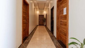 A hallway with wooden doors, a tiled floor, and a ceiling with recessed lighting. - Hotel Aaradhya Crown (Devgad)