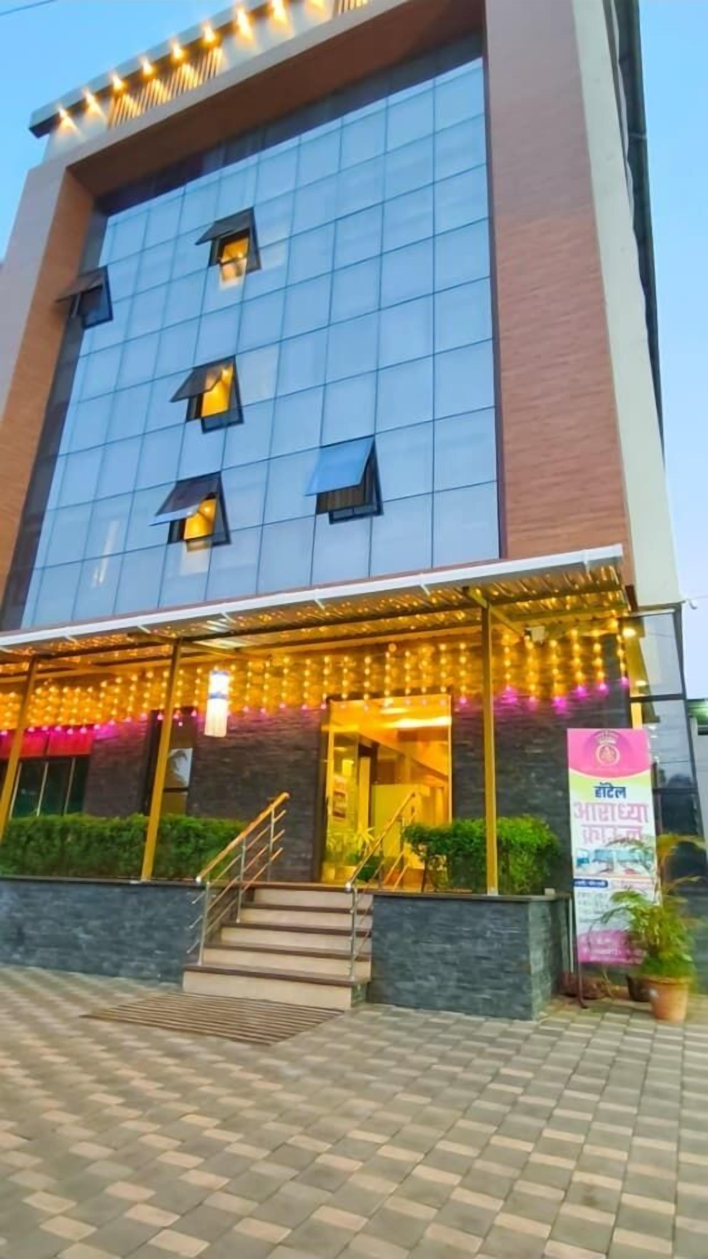 A modern hotel with a glass facade, a covered entrance area with string lights, and a staircase leading to the entrance.