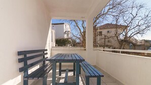 Ein Balkon mit einer Holzbank und einem Tisch, mit Blick auf ein Gebäude und Bäume.