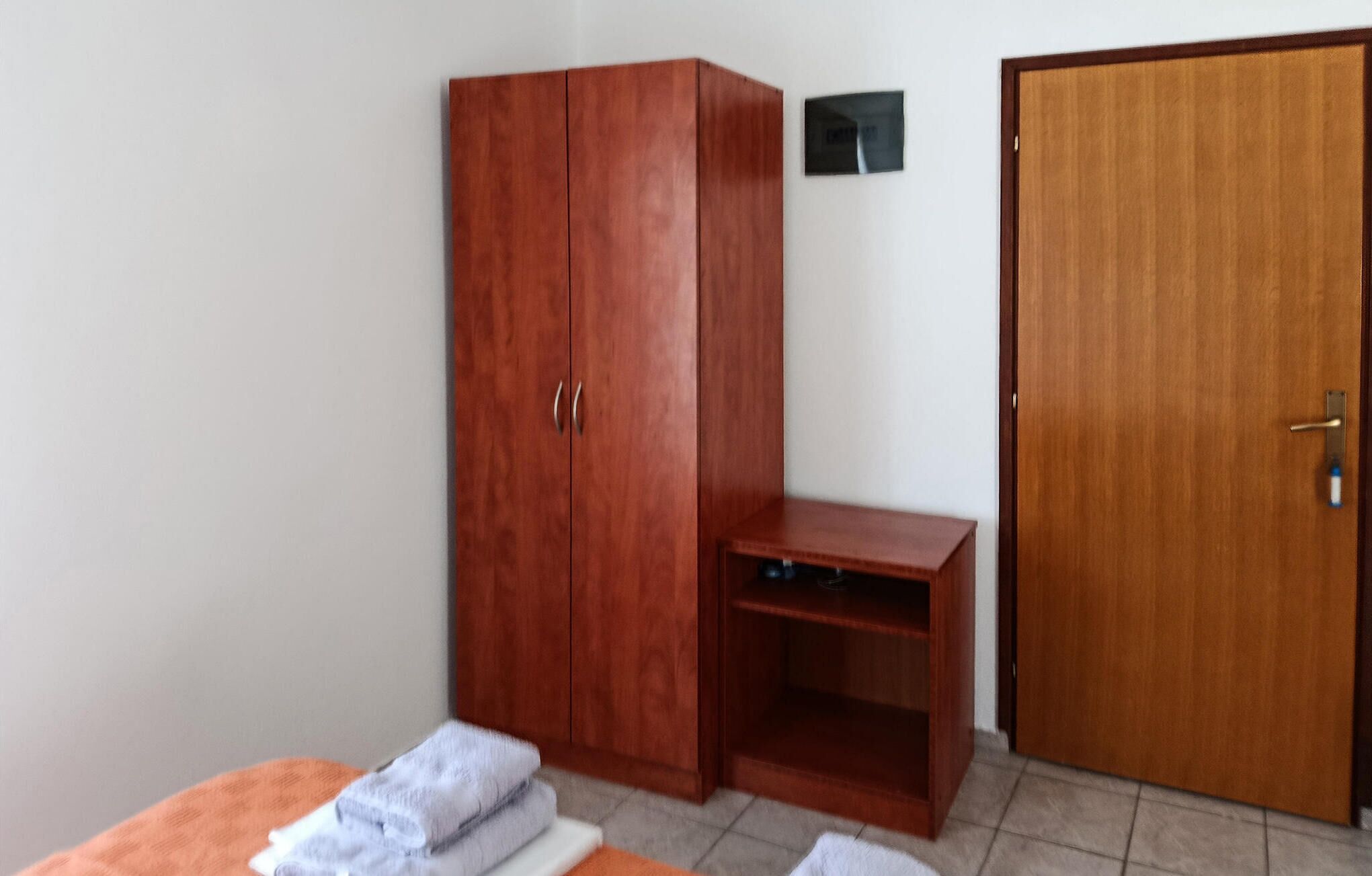 Quarto com guarda-roupa de madeira, uma pequena escrivaninha, uma porta e uma cama com toalhas.