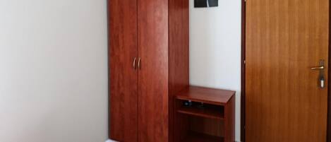 Quarto com guarda-roupa de madeira, uma pequena escrivaninha, uma porta e uma cama com toalhas.