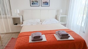 Een net opgemaakt bed met witte lakens, twee kussens en twee opgevouwen handdoeken op witte onderzetters.