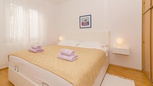 Een net opgemaakt bed met een beige deken, twee opgerolde handdoeken en een ingelijst foto aan de muur.